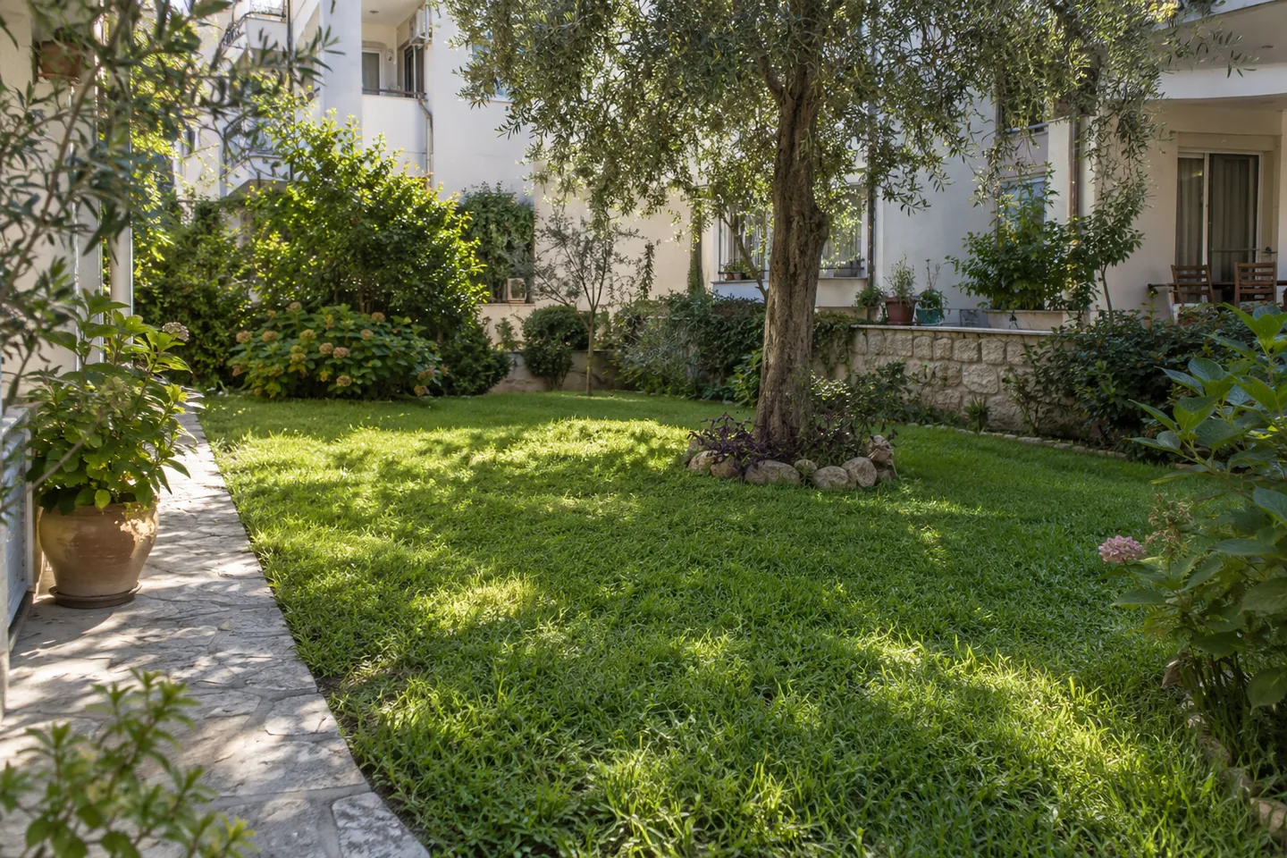 Apartman avlusunda ağaç gölgesi ve güneş alan çim bölümlerini gösteren temsili bahçe